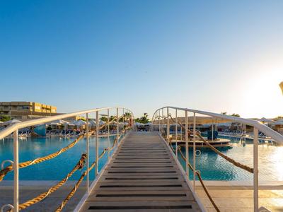 Steg führt über klares Wasser zu modernen Hotels bei Sonnenuntergang.