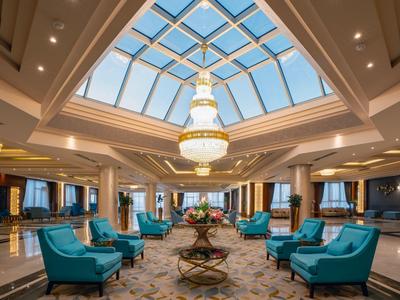 Hall d'hôtel élégant avec lustre et fauteuils bleus sous un plafond en verre.