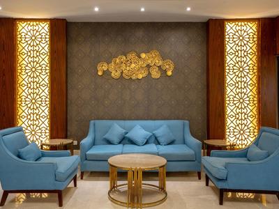 Espace lounge d'hôtel moderne avec canapé bleu, fauteuils et éléments décoratifs dorés.