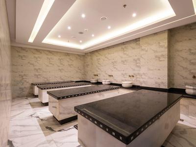 Salle de spa lumineuse avec murs en marbre, trois tables de massage et éclairage indirect au plafond.