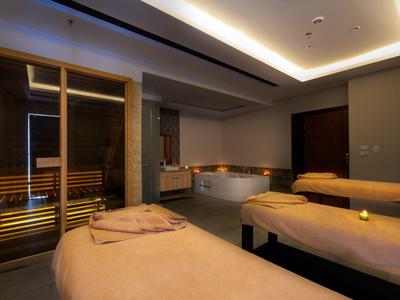 Une salle de spa luxueuse avec des tables de massage, des bougies et un sauna avec une façade en verre.