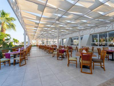 Freiluftrestaurant mit Holzmöbeln und überdachtem Bereich in sonniger Hotelanlage.