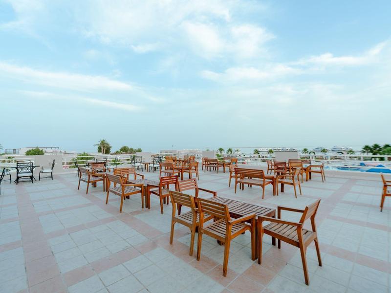 Terrasse vide avec tables et chaises en bois sous un ciel bleu près de la piscine de l'hôtel.