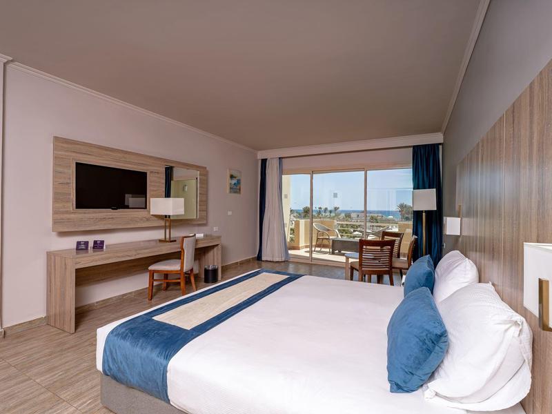 Chambre d'hôtel moderne avec grand lit, bureau, chaises et balcon avec vue sur la mer.