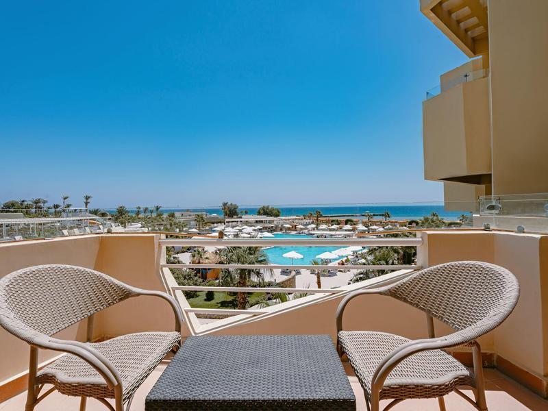 Balcon avec deux chaises donnant sur la piscine et la mer sous un ciel clair.