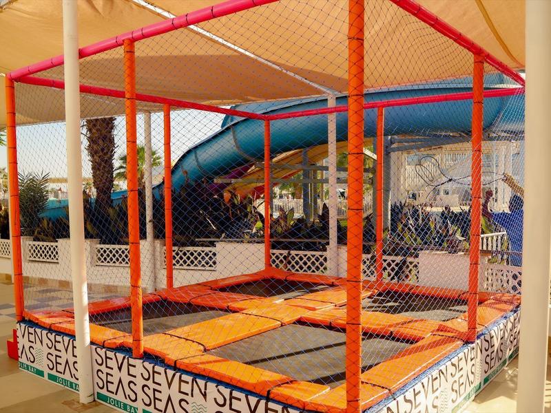 Zone de trampoline colorée avec enceinte en filet et toboggan bleu en extérieur.