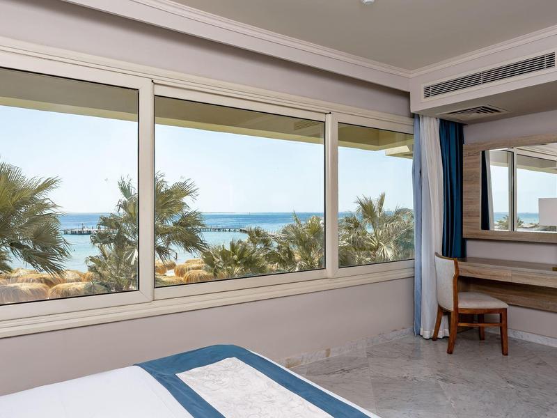 Chambre d'hôtel avec vue sur la mer, grandes fenêtres, palmiers à l'extérieur et un bureau avec chaise