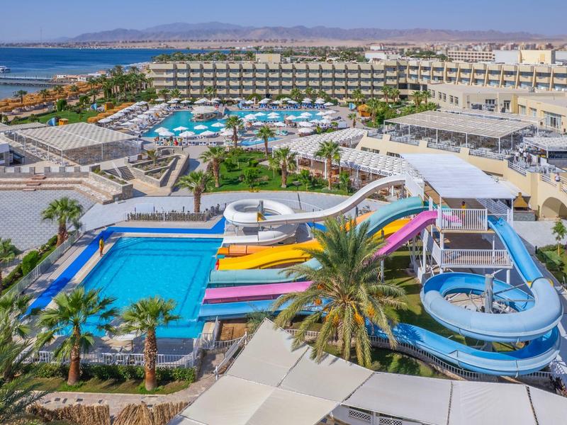 Vue d'un hôtel avec toboggans aquatiques, piscines et la mer en arrière-plan.