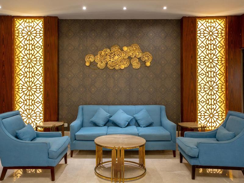 Espace lounge d'hôtel moderne avec canapé bleu, fauteuils et éléments décoratifs dorés.