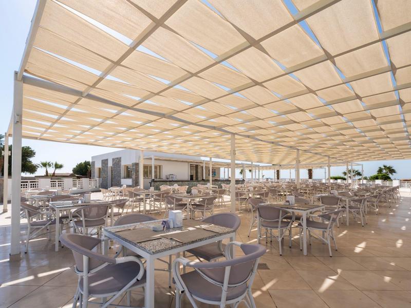 Grand espace extérieur de restaurant avec de nombreuses tables et chaises sous un grand auvent.