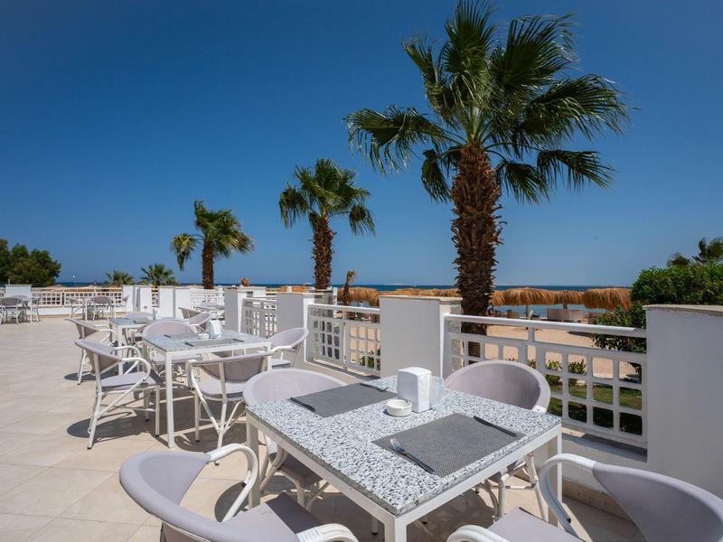 Terrasse avec des tables et chaises blanches sous un ciel bleu avec des palmiers en arrière-plan.