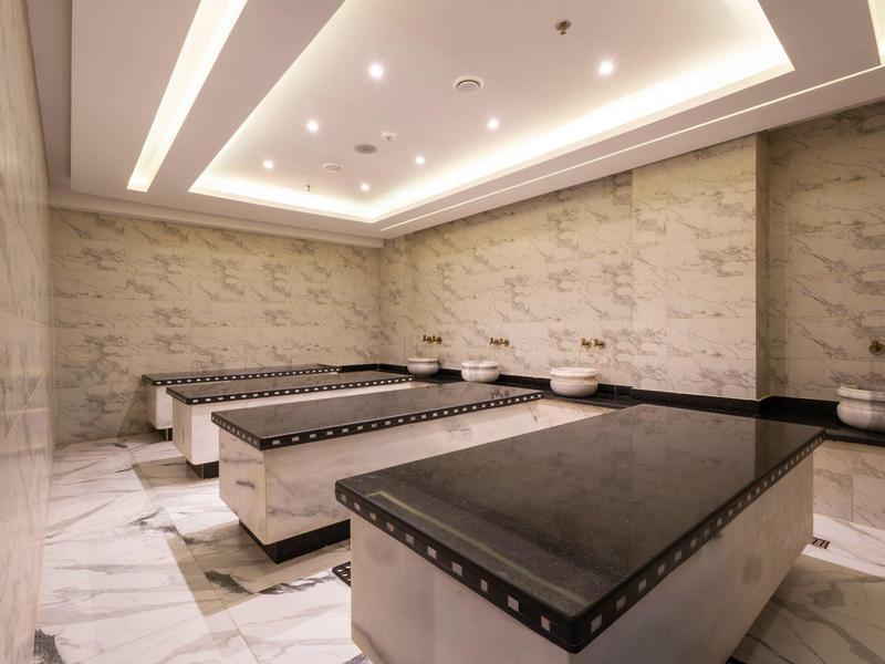 Salle de spa lumineuse avec murs en marbre, trois tables de massage et éclairage indirect au plafond.