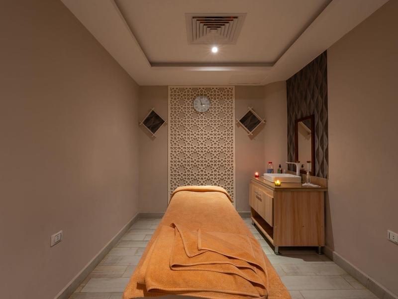 Chambre de spa simple avec table de massage, couverture orange et meuble en bois contre le mur.