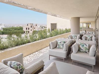 Moderní balkon s pohodlnými křesly a květinovými polštáři, výhled na zeleň a město.