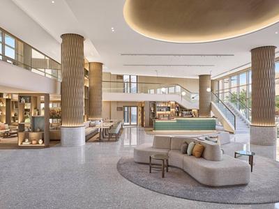 Bright hotel lobby with modern furnishings, large windows, and seating areas.