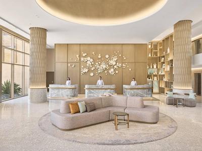 Spacious hotel lobby with modern sofa, reception desks, and decorative wooden panels.
