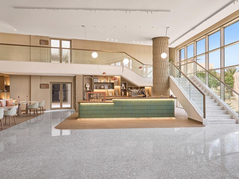 Hall lumineuse avec grandes fenêtres, banc et escalier au design minimaliste.