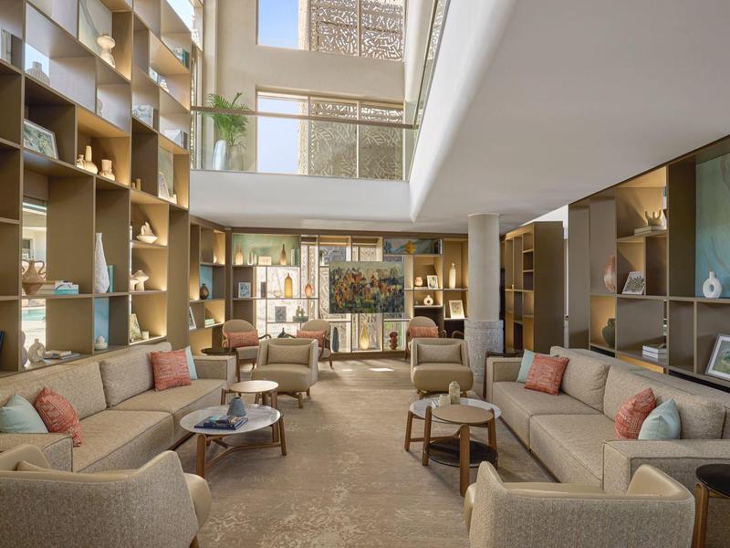 Grand salon d'hôtel lumineux avec canapés modernes et étagères décoratives.