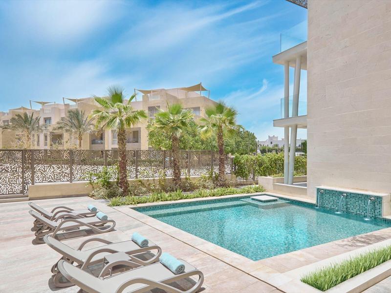 Espace piscine extérieure moderne avec chaises longues et palmiers par une journée ensoleillée.