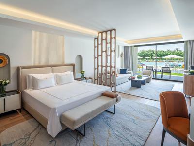 Bright hotel room with large bed, wooden accents, and terrace seating overlooking greenery.