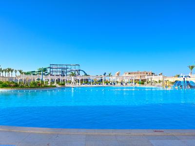 Grande piscine extérieure avec eau bleue claire et espaces détente alentours sous ciel bleu.