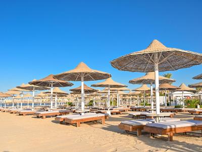 Plage avec rangées de parasols en paille et transats sous un ciel bleu clair