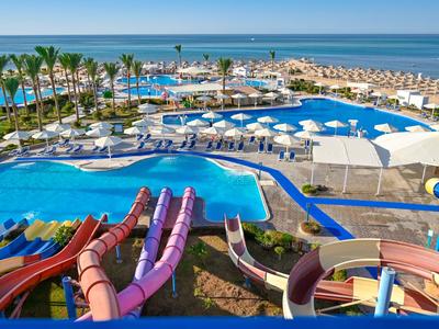 Vue d'un parc aquatique avec des toboggans, une piscine, des chaises longues et la mer en arrière-plan.