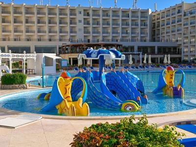 Piscina con toboganes azules y amarillos en un hotel grande bajo cielo despejado