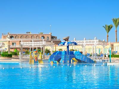 Gran piscina con toboganes de agua y edificios de hotel bajo un cielo despejado y palmeras al fondo.