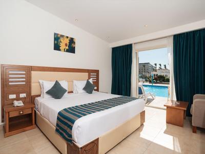 Habitación de hotel luminosa con cama doble, muebles de madera y acceso a una zona de piscina mediante una puerta corredera de cristal.