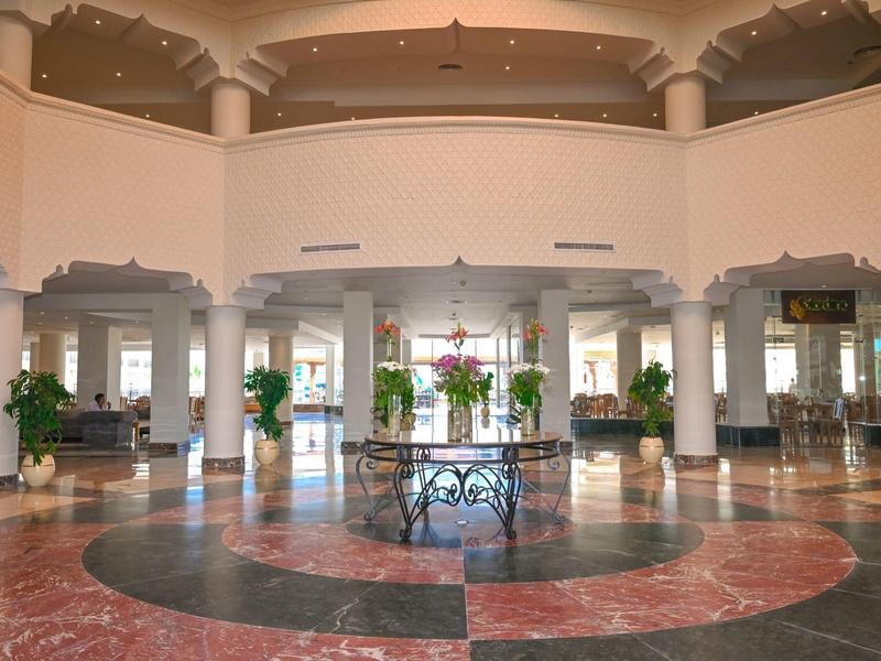 Vestíbulo espacioso de hotel con suelo de mármol, columnas y una mesa redonda con flores en el centro.