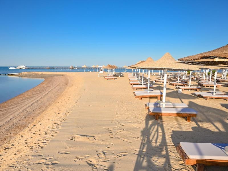 Playa de arena vacía con tumbonas y sombrillas en un día tranquilo y despejado.