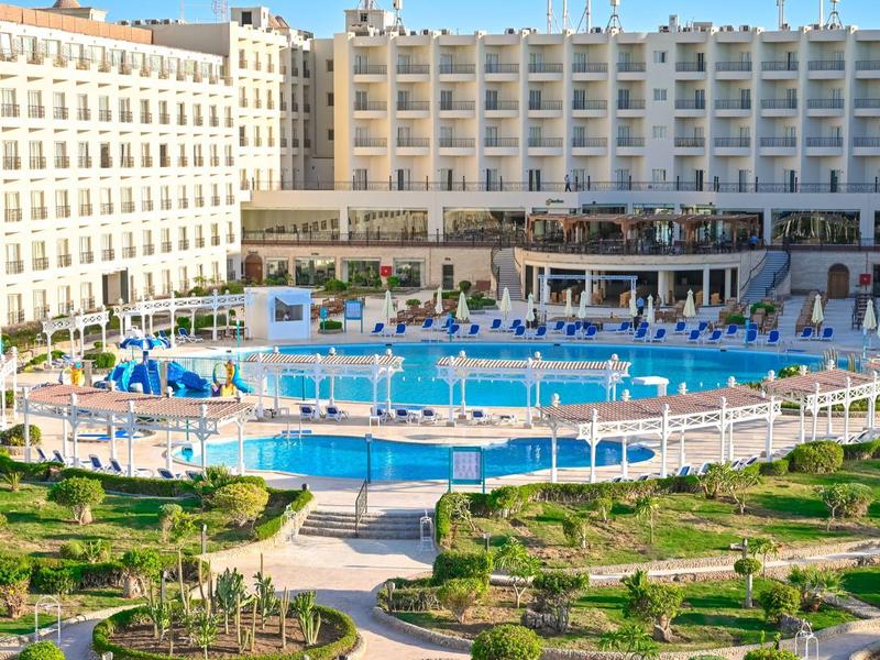 Gran complejo hotelero con piscina al aire libre y jardín cuidado en ubicación soleada.