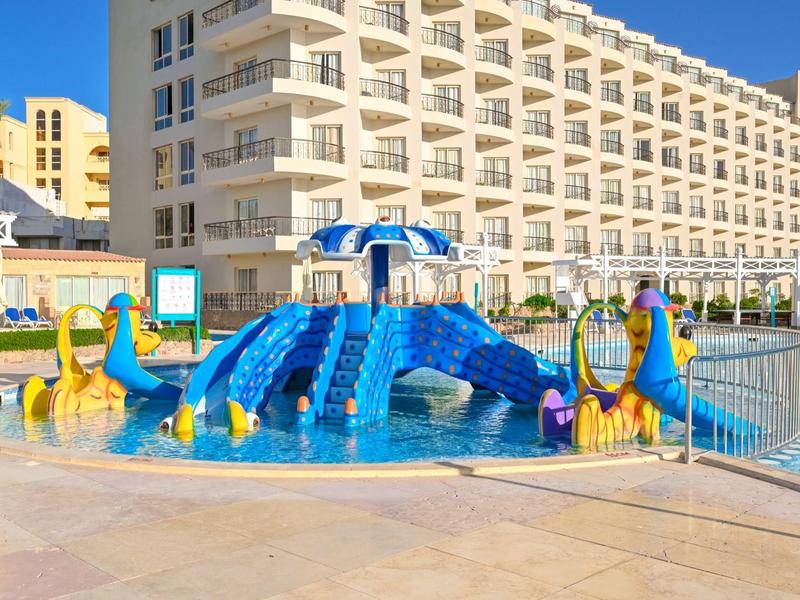 Colorida zona de juegos acuáticos para niños con toboganes en la piscina frente a un gran hotel.