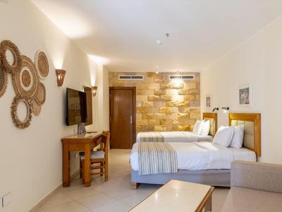 Chambre d'hôtel lumineuse avec deux lits, mobilier en bois et éclairage mural décoratif.