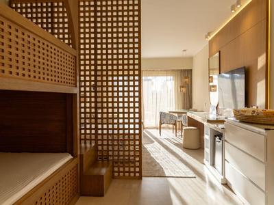 Chambre d'hôtel lumineuse avec séparateur de pièce en bois et meubles aux tons naturels.