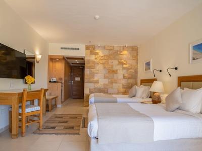 Chambre d'hôtel lumineuse avec deux lits, bureau et télévision.