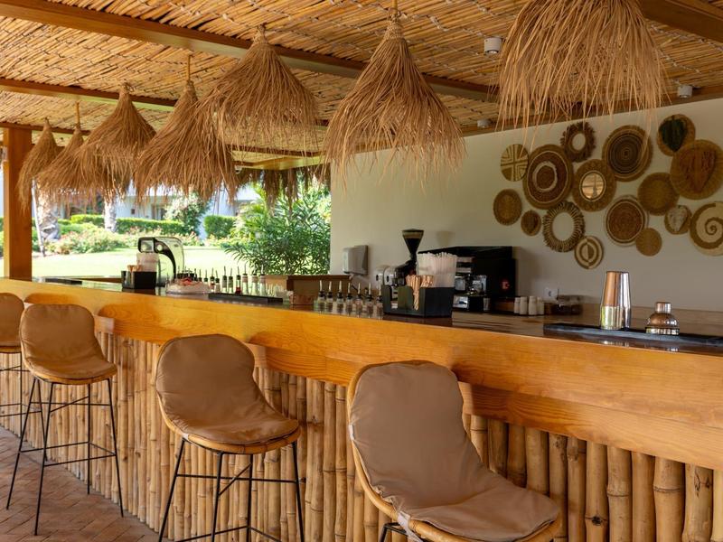 Bar confortable avec comptoir en bois, chaises hautes et lampes décoratives sous un toit de chaume.