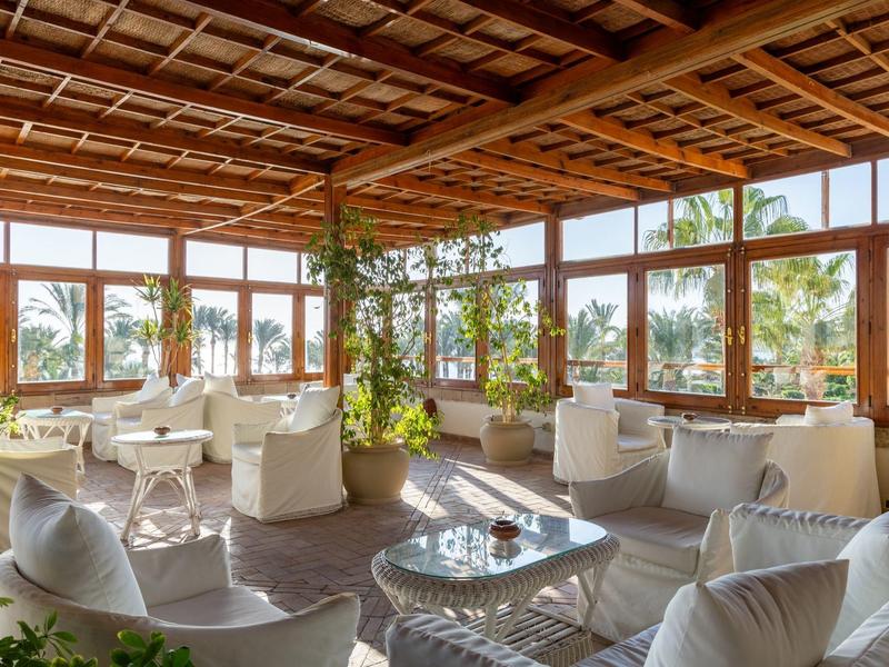 Salon lumineux avec meubles blancs et grandes fenêtres donnant sur des palmiers.