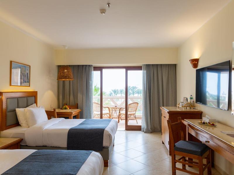 Chambre d'hôtel lumineuse avec deux lits simples et balcon avec vue sur l'eau.