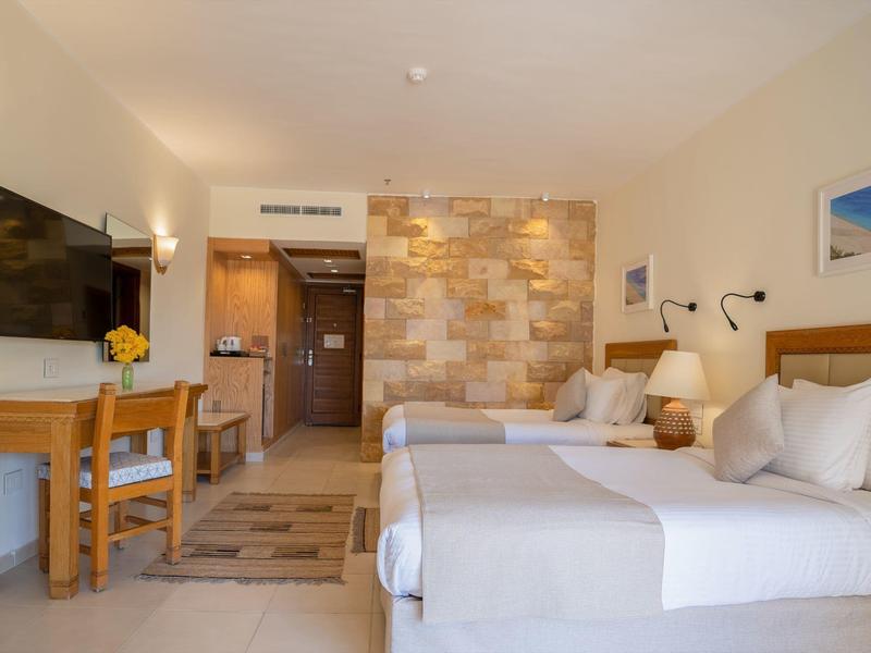 Chambre d'hôtel lumineuse avec deux lits, bureau et télévision.