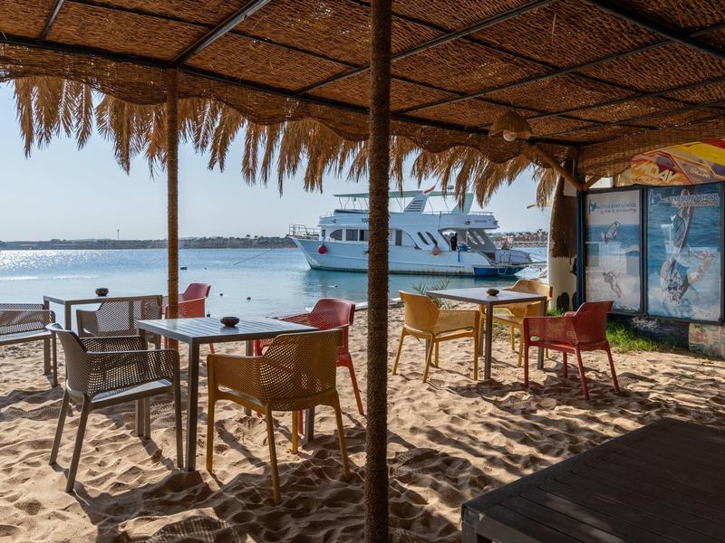 Coin de cabane de plage ensoleillé avec chaises et tables au bord de l'eau.
