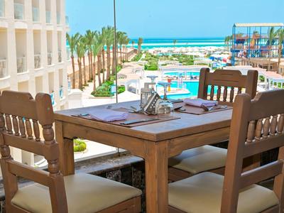 Widok z drewnianego stołu z krzesłami na basen hotelowy i morze w tle.