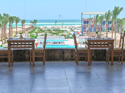 Vue sur une piscine avec des chaises longues, des palmiers et la mer en arrière-plan par une journée ensoleillée