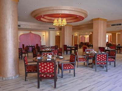 Przestronny hotelowy obszar restauracyjny z wieloma stołami i krzesłami, ciepłe oświetlenie i harmonijne kolory.