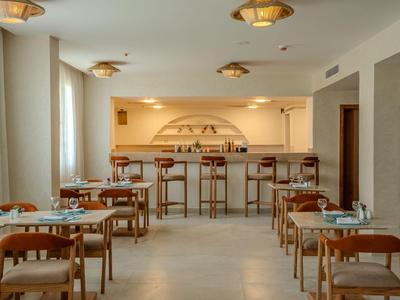 Bright, modern restaurant with wooden tables, chairs, and a bar in the background.