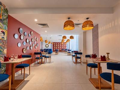 Modern hotel restaurant with colorful chairs, round wall mirrors, and hanging lights.