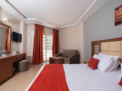 Chambre d'hôtel moderne avec lit double, jetée rouge, canapé et balcon.