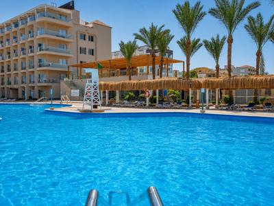 Large blue pool in front of a hotel with palm trees and sun umbrellas on the pool terrace.