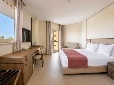 Bright hotel room with double bed, wooden furniture, and balcony with outdoor view.